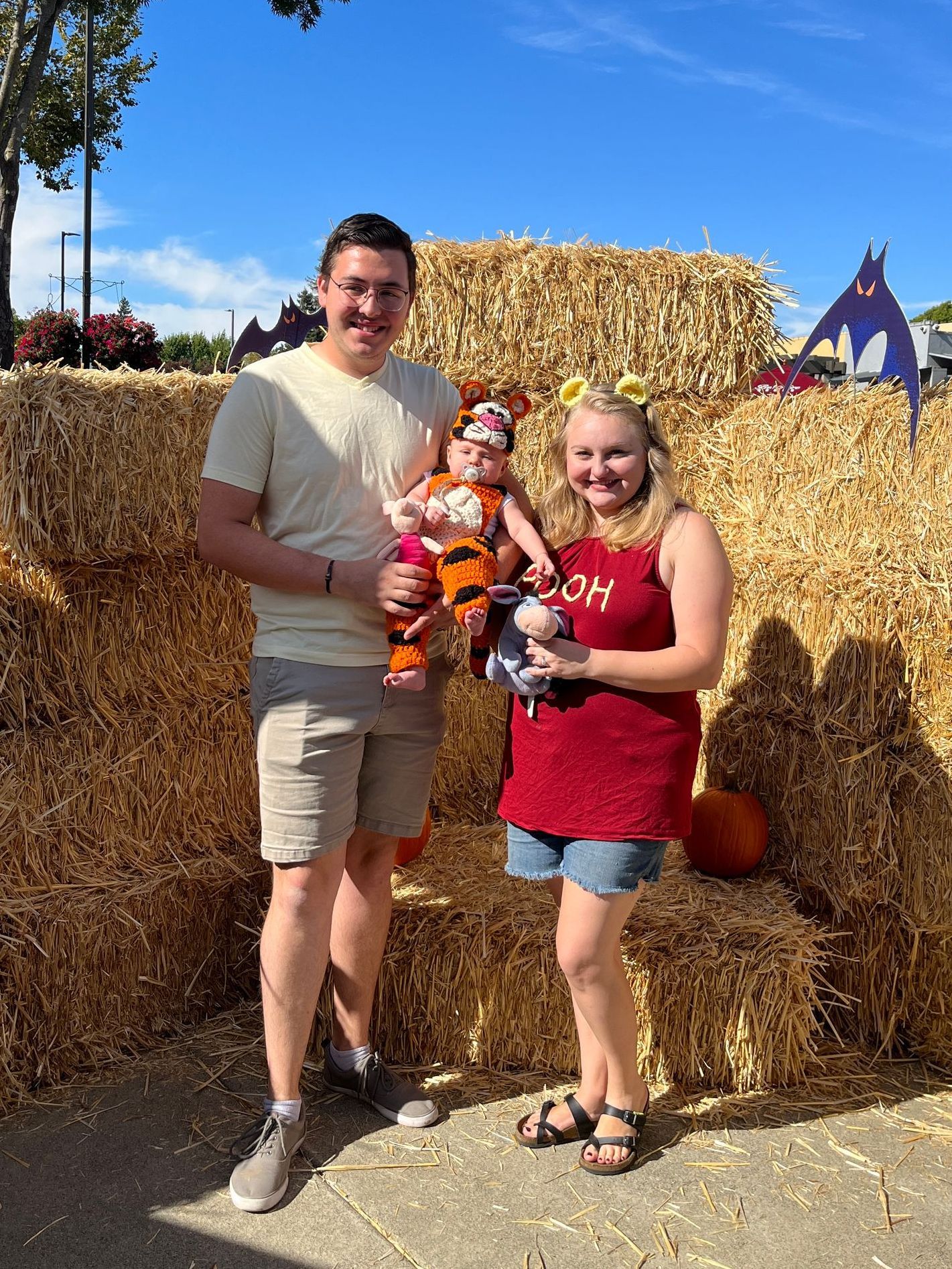 A man , woman and baby are posing for a picture in front of hay bales.
