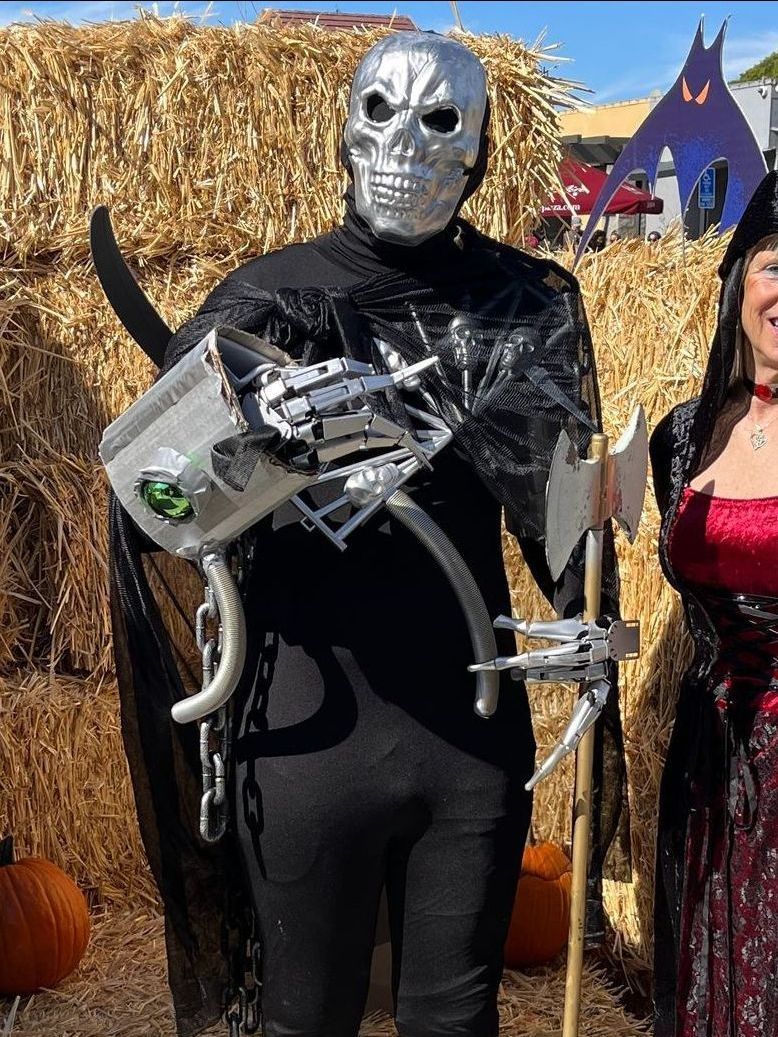 A man in a skeleton costume is standing next to a woman in a witch costume.