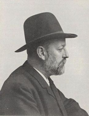 Zwart-wit profielportret van een bebaarde man met een breedgerande hoed en een pak.