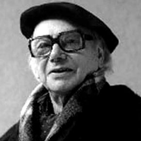 Zwart-wit portret van een persoon met een baret, bril en sjaal, die iets omhoog kijkt.