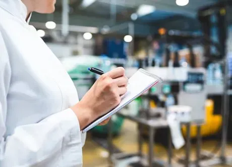 Person in a white coat writing on a clipboard in a laboratory.