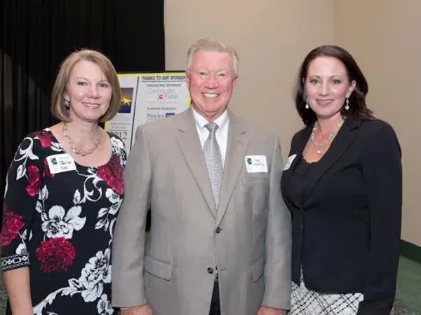 Three people posing indoors at a formal event, smiling at the camera.