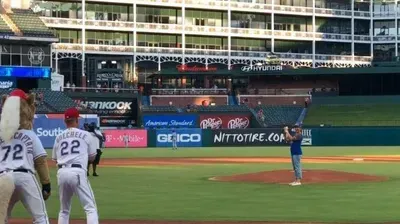 Baseball field with players near home plate and a pitcher on the mound in a stadium