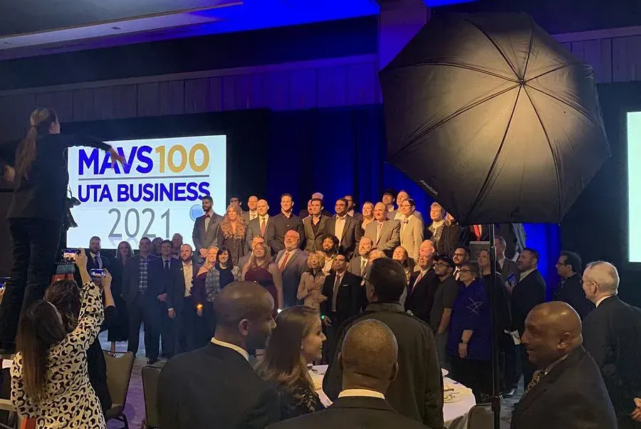 Award ceremony group photo on stage with a blue-lit backdrop and a sign reading “MVS100 FUTA BUSINESS 2021”