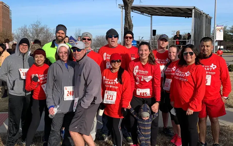 Group of runners in red shirts posing together at a start line outdoors.