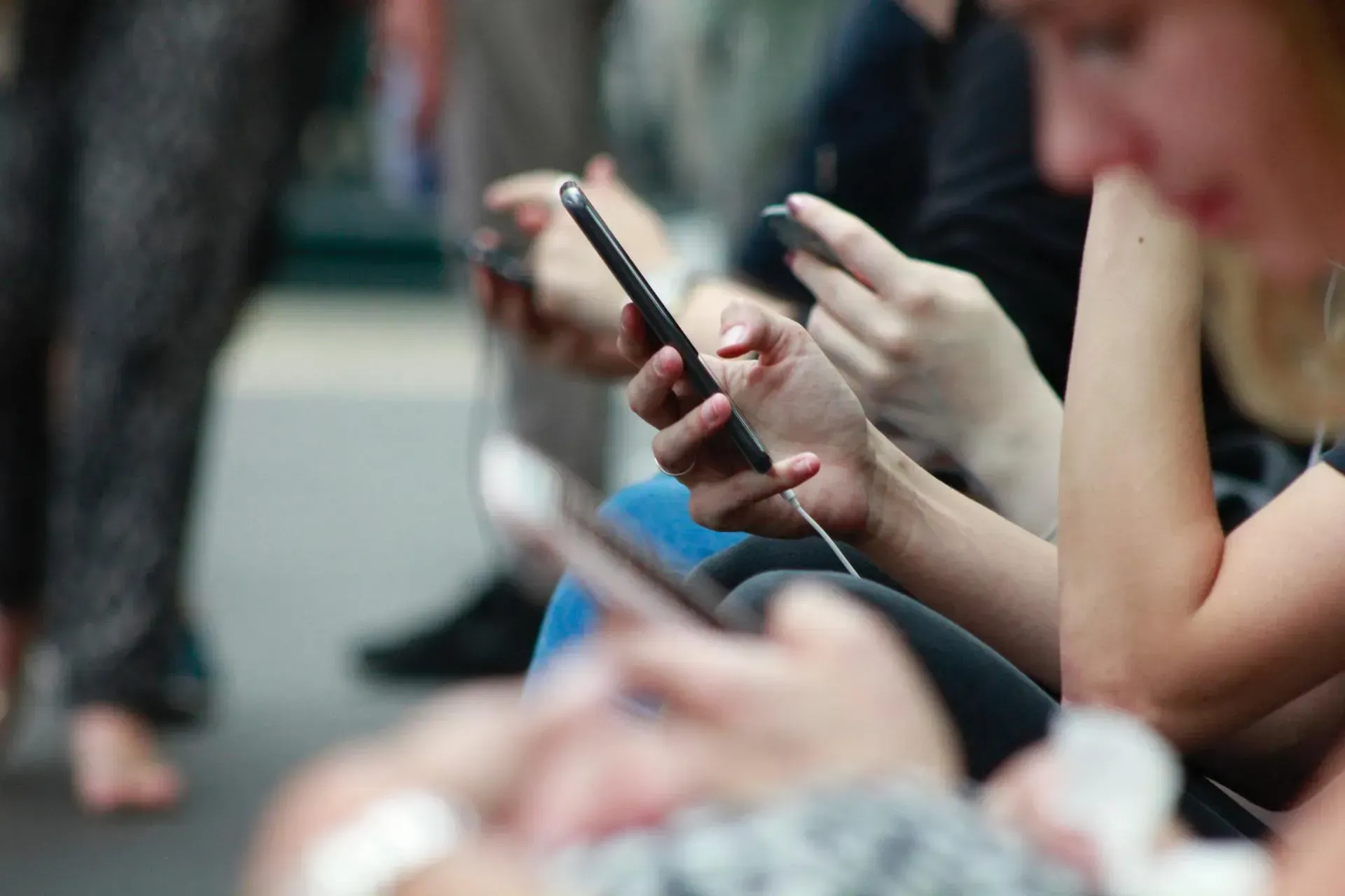 People seated outdoors, all looking at and using smartphones.