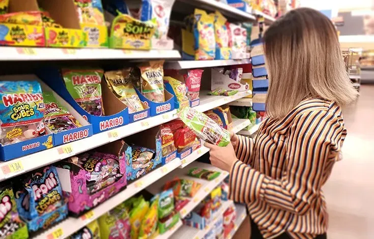 Woman shopping in a candy aisle, reaching for colorful snacks on store shelves.