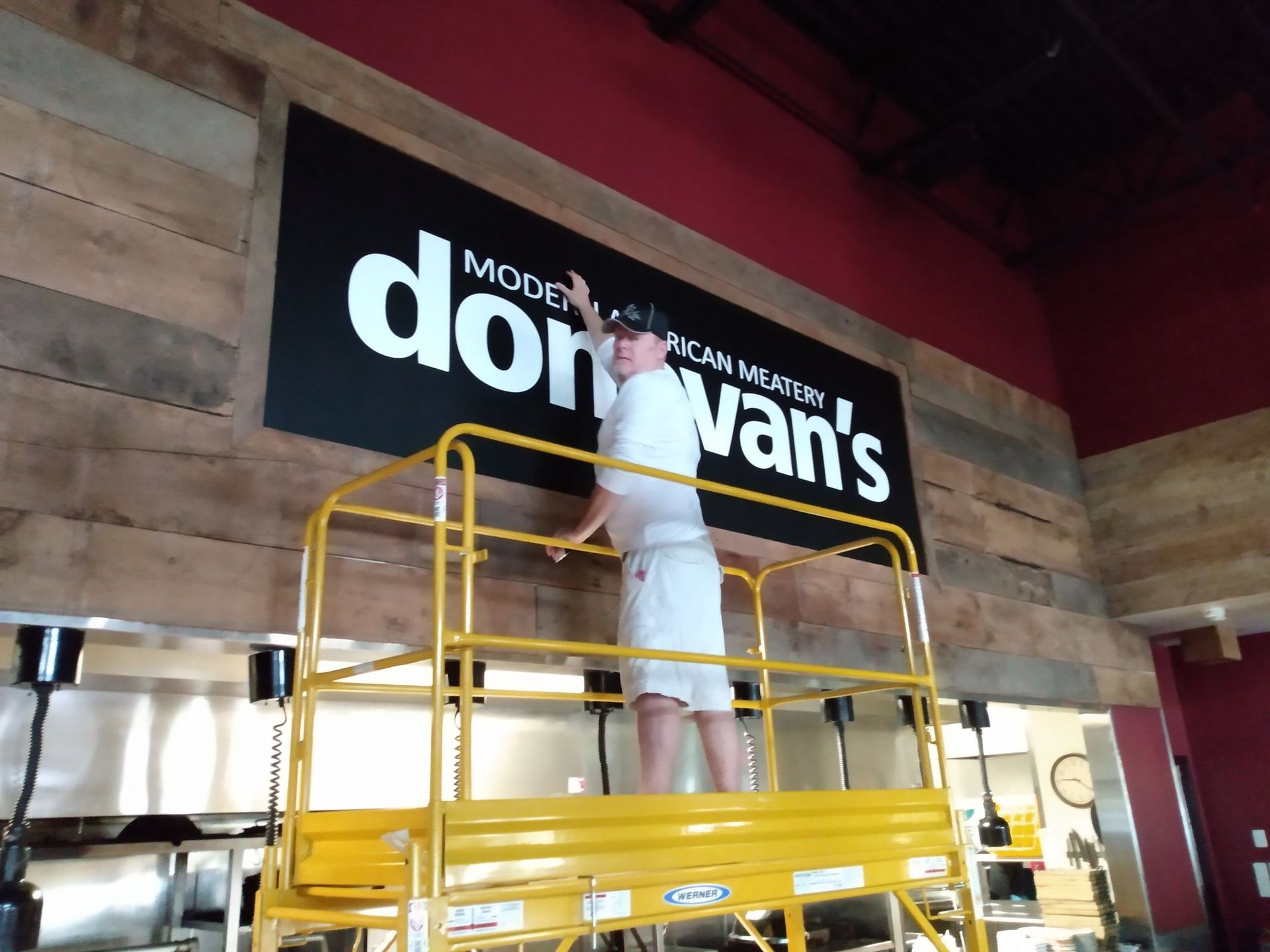 A man is standing on a ladder in front of a sign that says don van 's