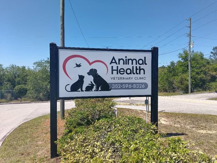 A sign for animal health veterinary clinic is sitting on the side of the road.