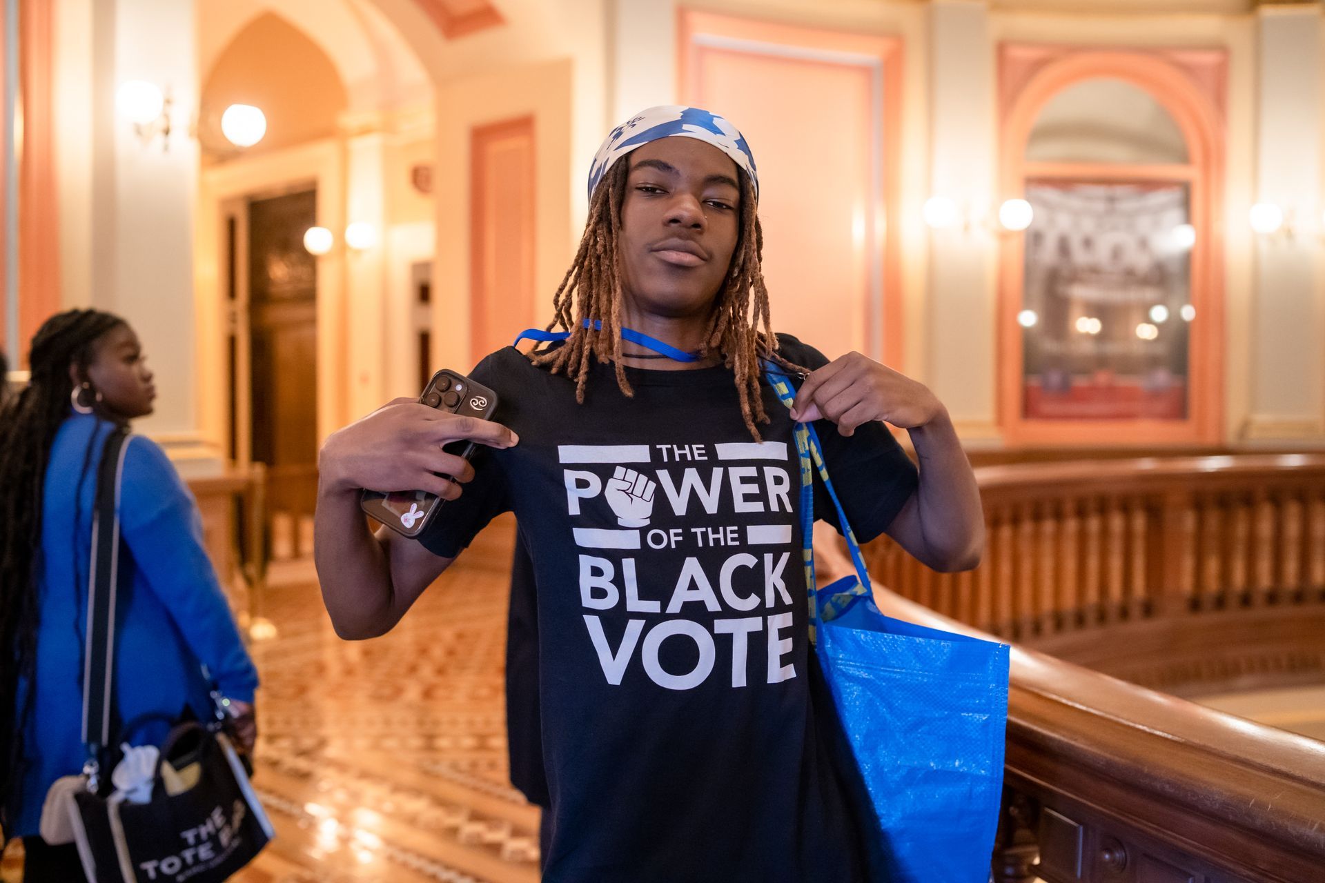 Person holding a black “Power to the Black Vote” shirt in a grand indoor hall