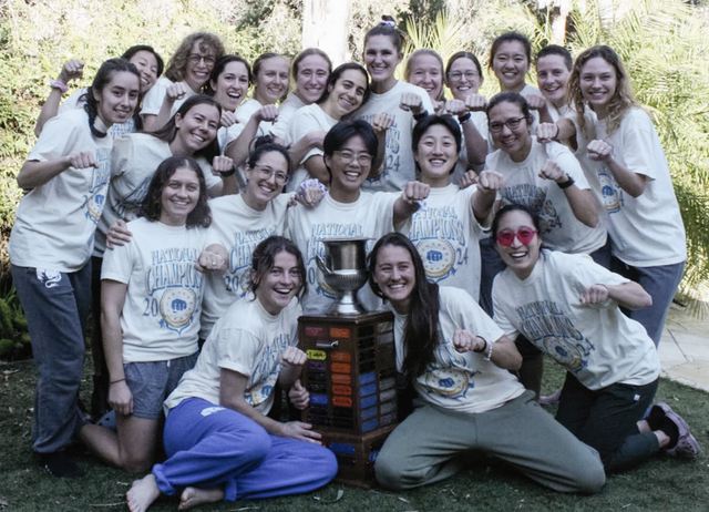 Group of smiling people in white shirts posing outdoors around a colorful stacked cube sculpture.
