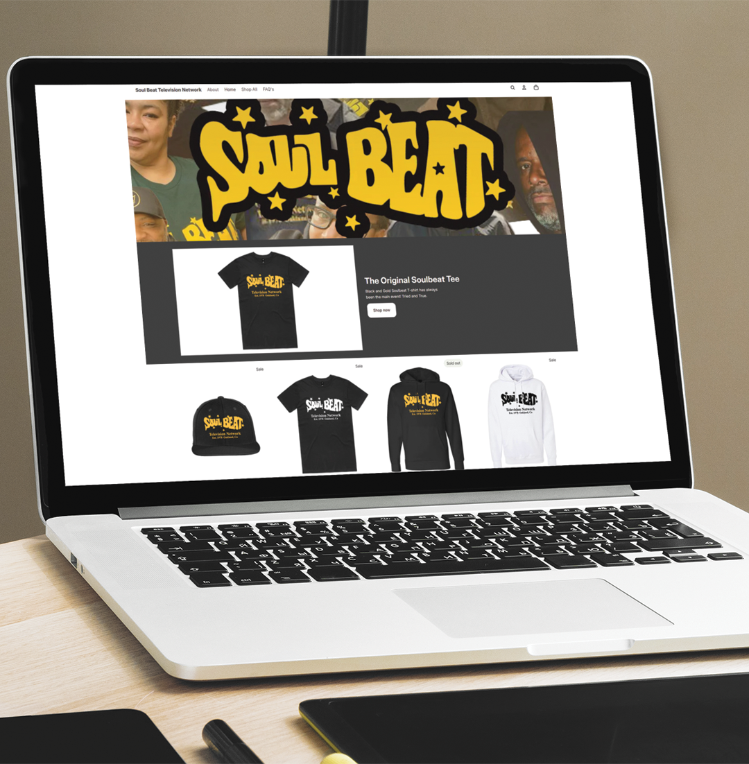Laptop displaying a Soul Beat merchandise store with black and yellow T-shirts on a white desk