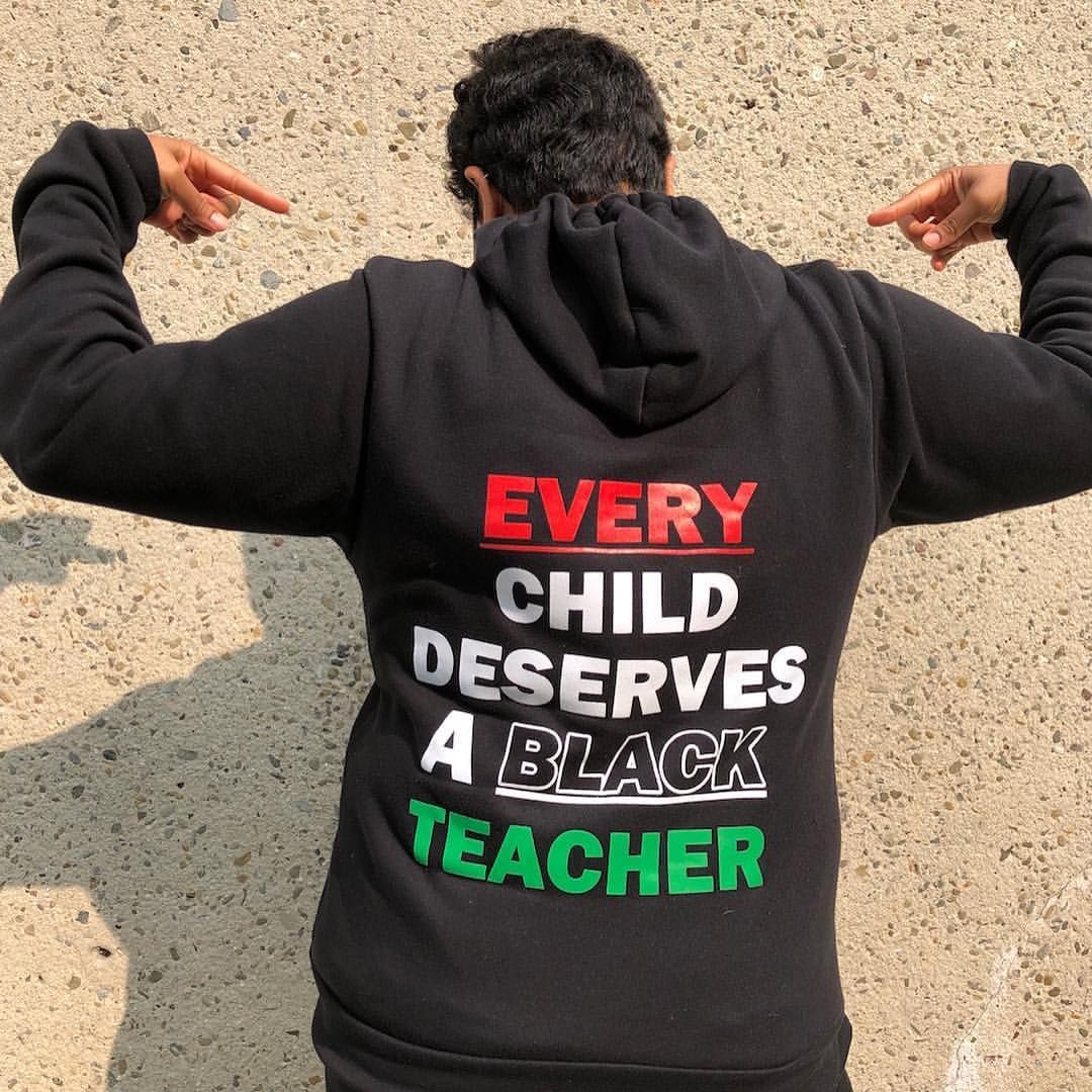 Person in black hoodie pointing to text: “Every child deserves a black teacher.”