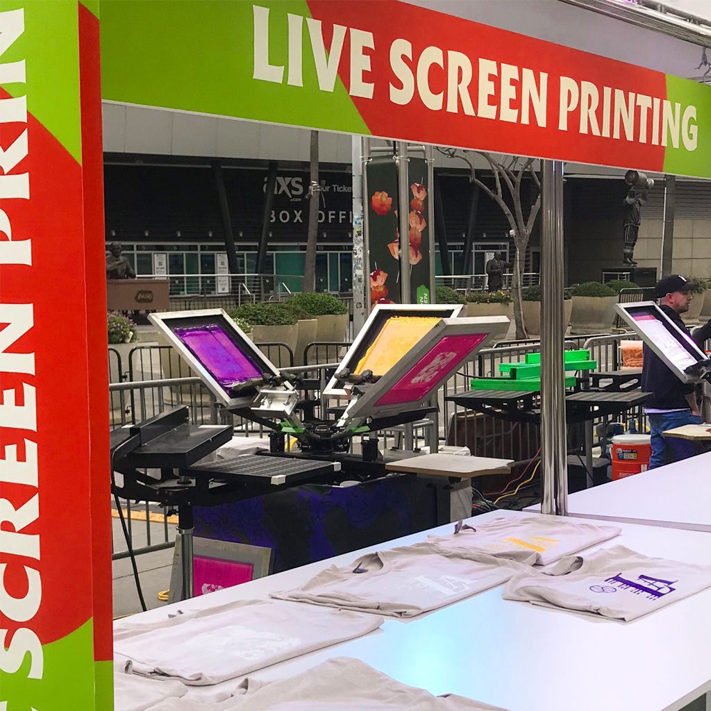 Live screen printing booth with colorful press equipment and printed T-shirts on display