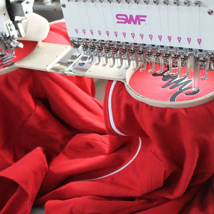 Embroidery machine stitching red fabric with pink thread and a curved design