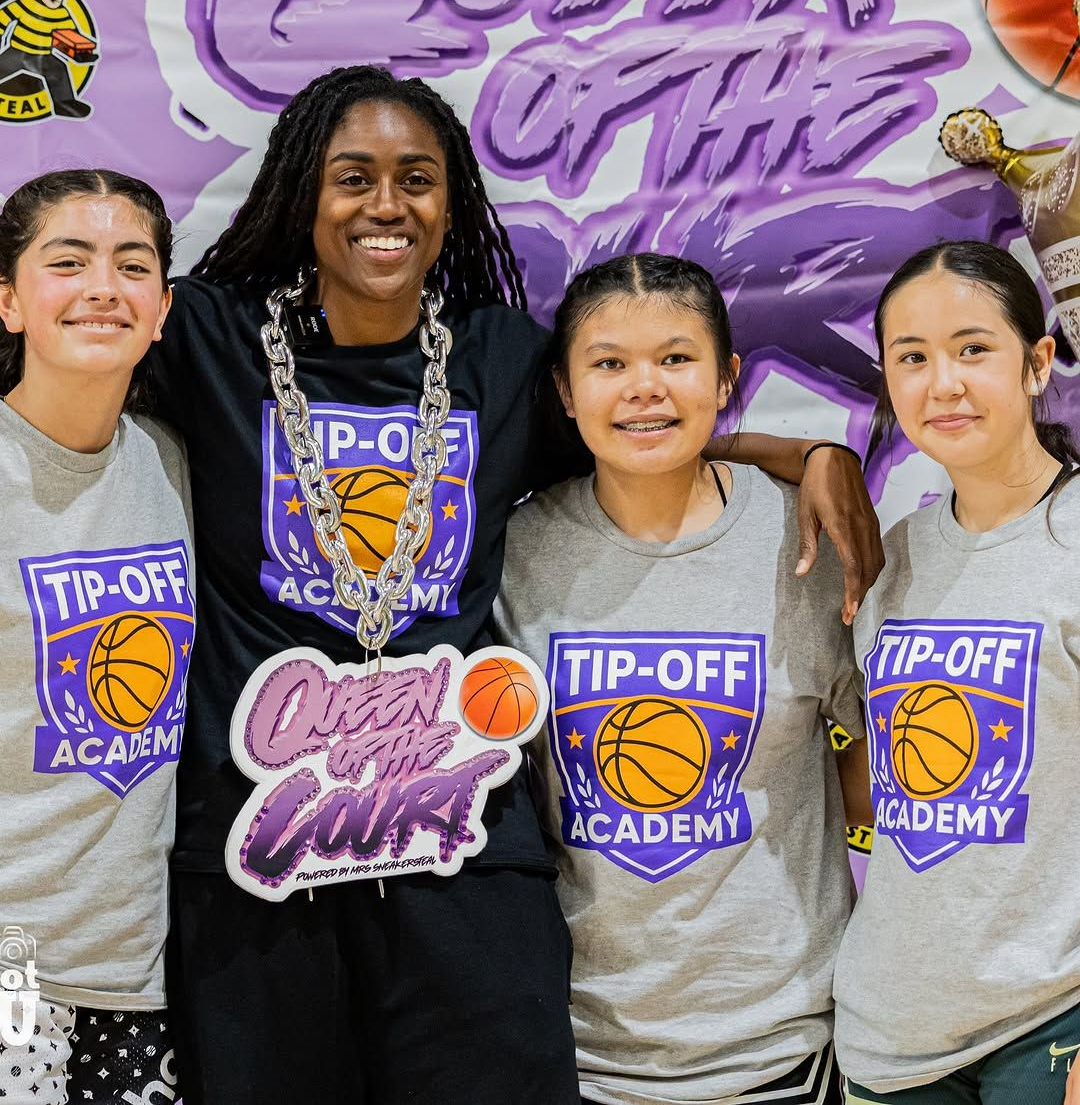 Four basketball academy members posing in front of a purple Tip-Off Academy mural, smiling in team shirts and medals