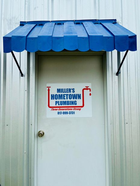 White door with Miller's Hometown Plumbing sign, blue awning, metal siding.
