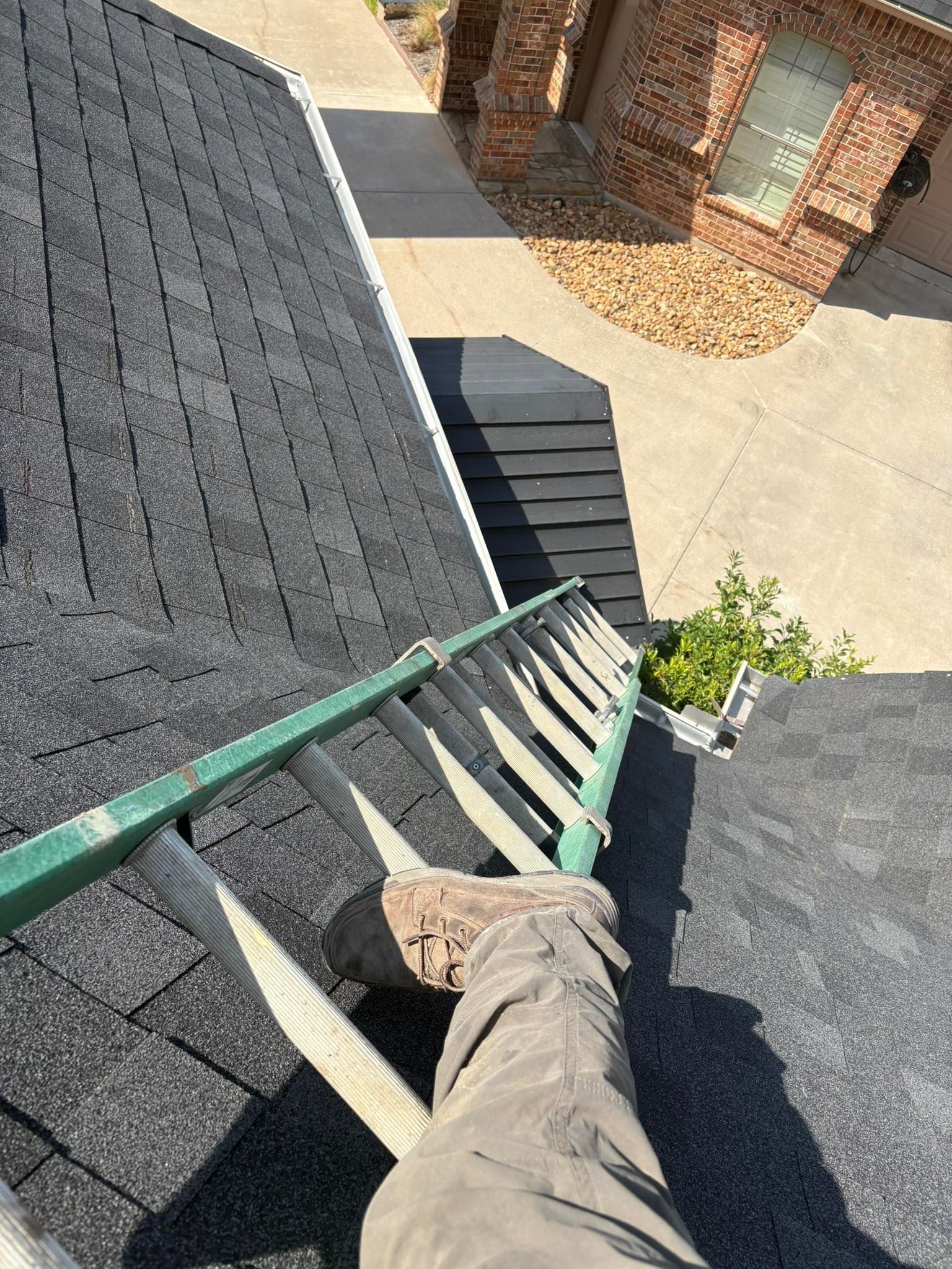 A person on a ladder on a roof, inspecting the gutter.