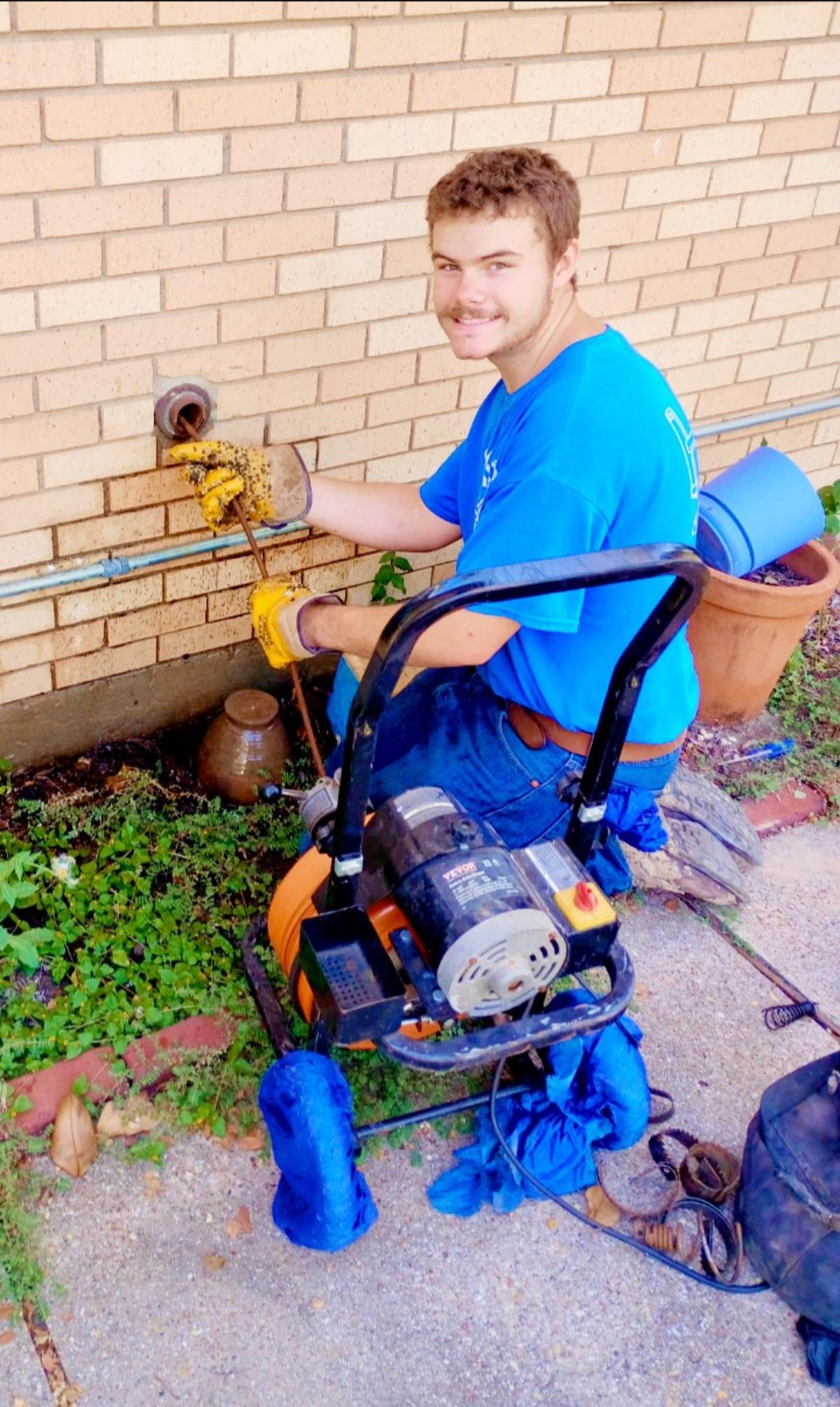 Man in blue shirt, kneeling by brick wall, using a pressure washer.