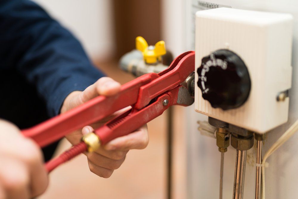 A Person is Fixing a Water Heater With a Wrench — Mid Richmond Plumbers & Suppliers in Alstonville, NSW