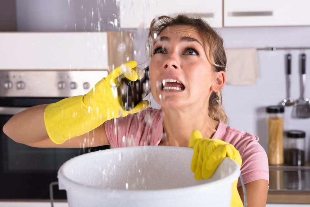 A Woman is Holding a Bucket With Water Coming Out of the Ceiling — Mid Richmond Plumbers & Suppliers in Coraki, NSW