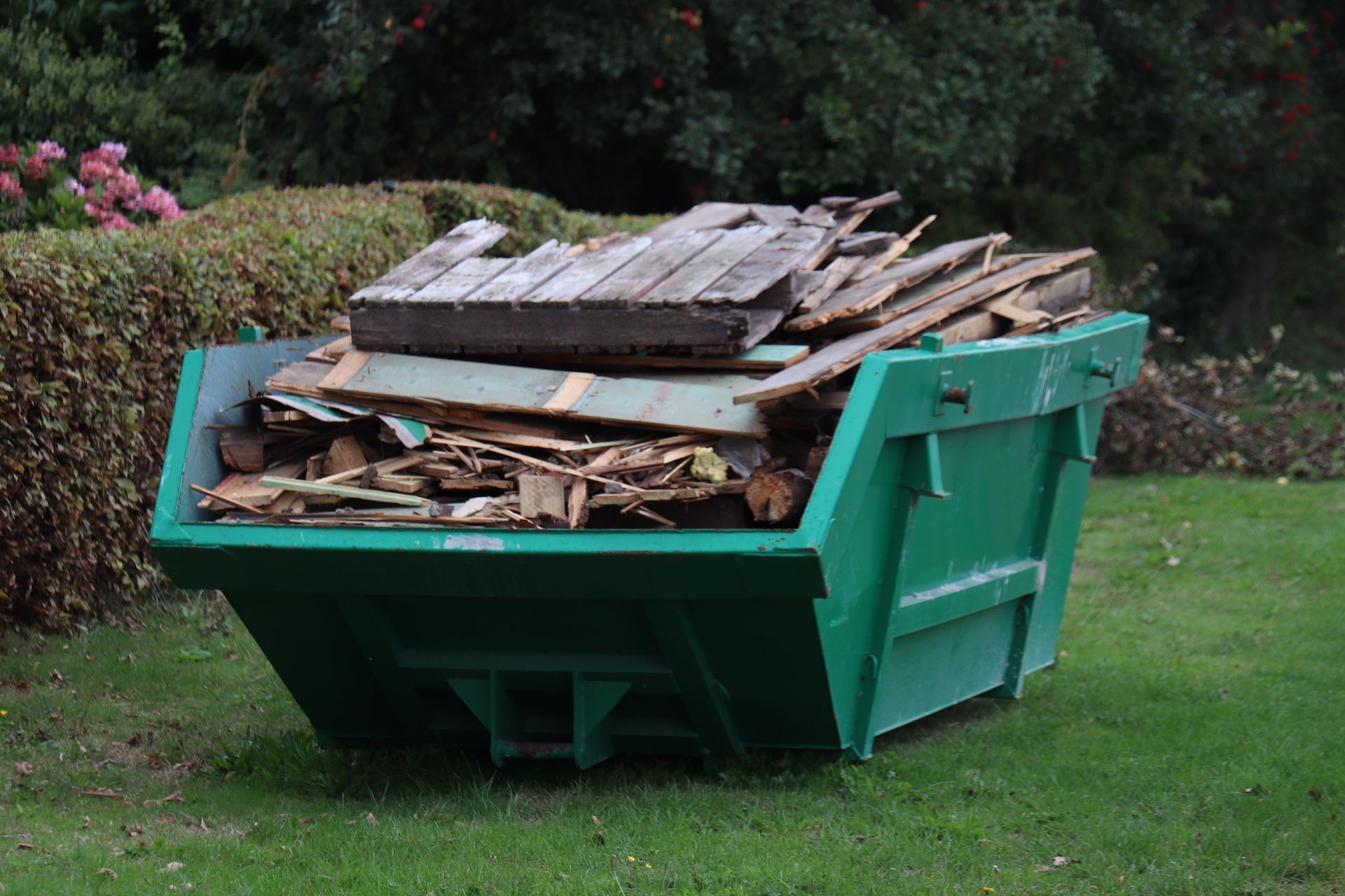 Green dumpster filled with broken wood and debris on a grassy lawn