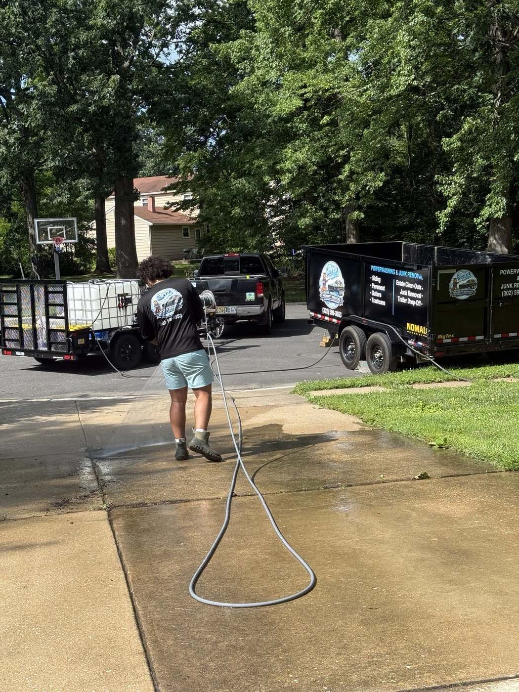 Technician pressure washing a driveway with branded equipment trailers in the background