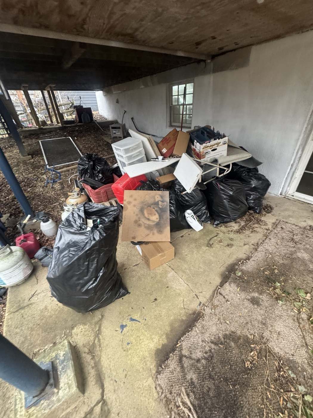 Bagged junk and household clutter piled under a deck ready for removal