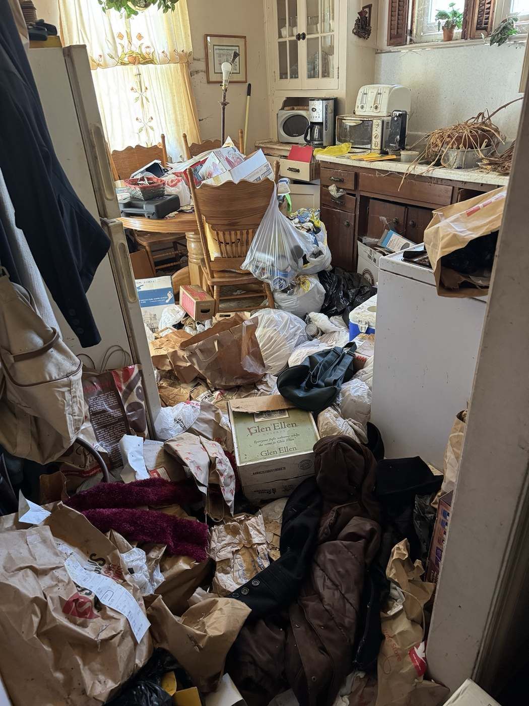 Cluttered kitchen and dining area full of bags and boxes before an estate cleanout