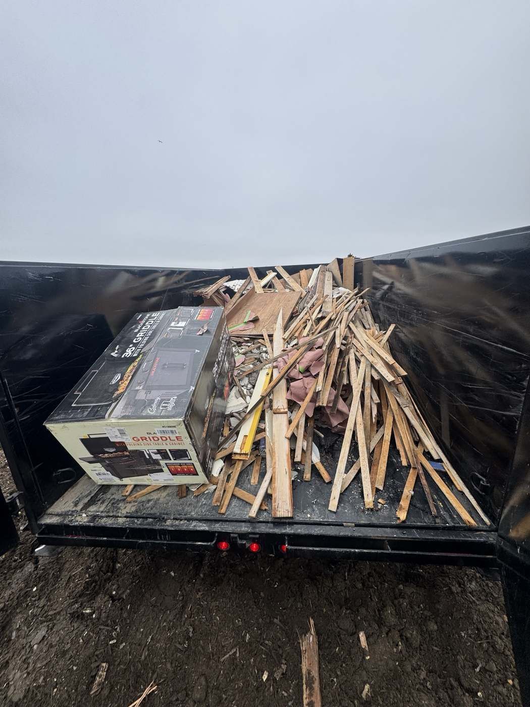 Trailer loaded with wood scraps and a boxed grill for junk removal