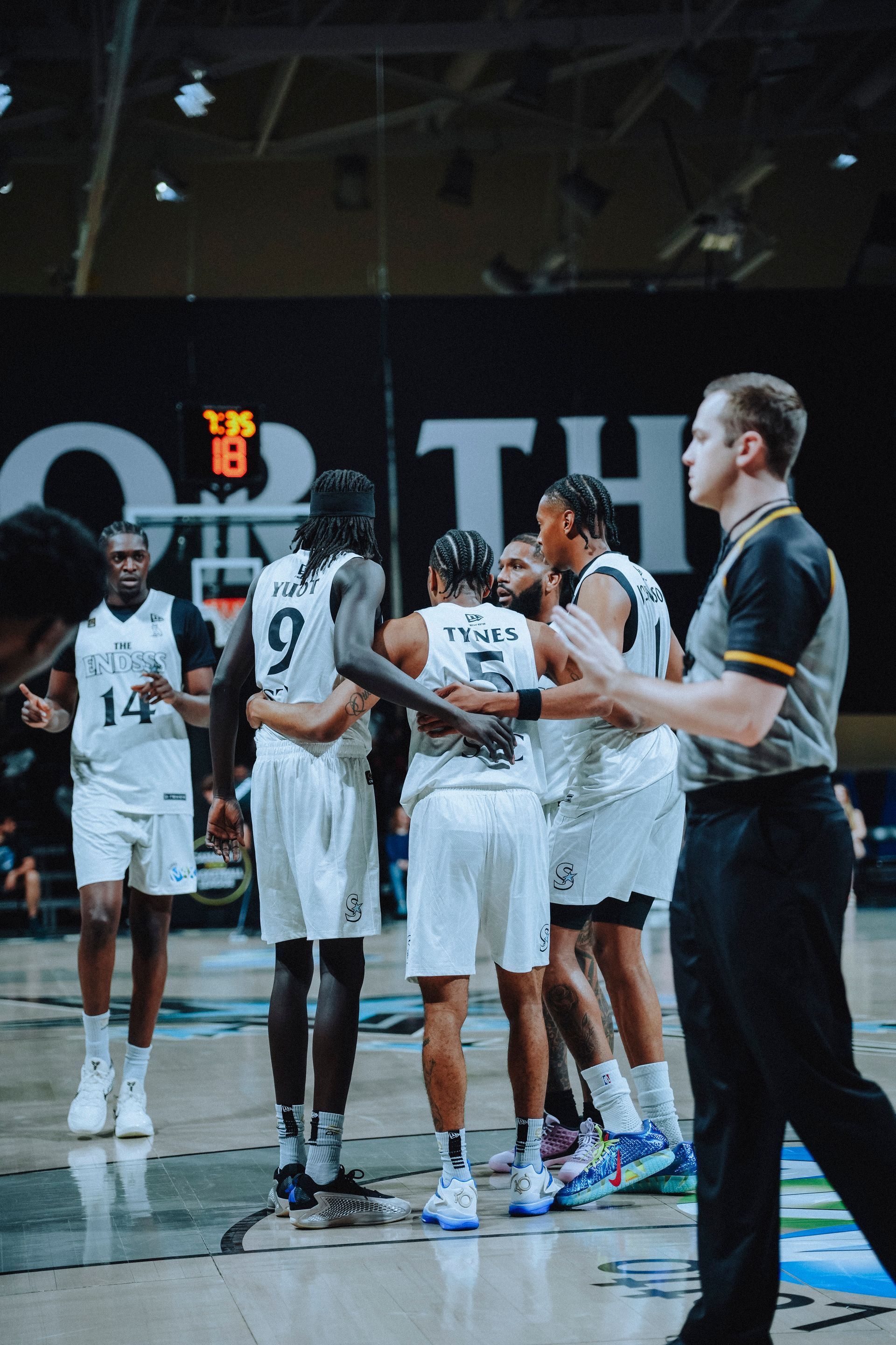 5 basketball players rally for a quick huddle during a stoppage in play
