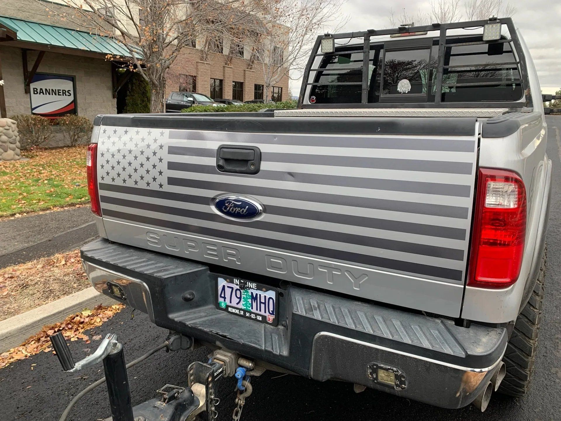 A silver ford truck with an american flag on the tailgate is parked in a parking lot.