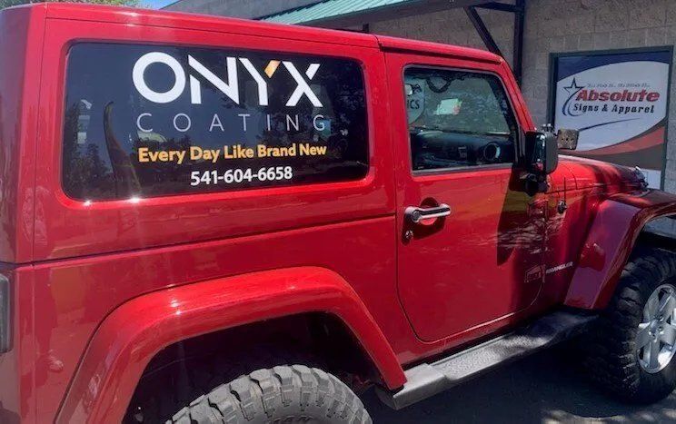A red jeep with onyx coating written on the side is parked in front of a building.
