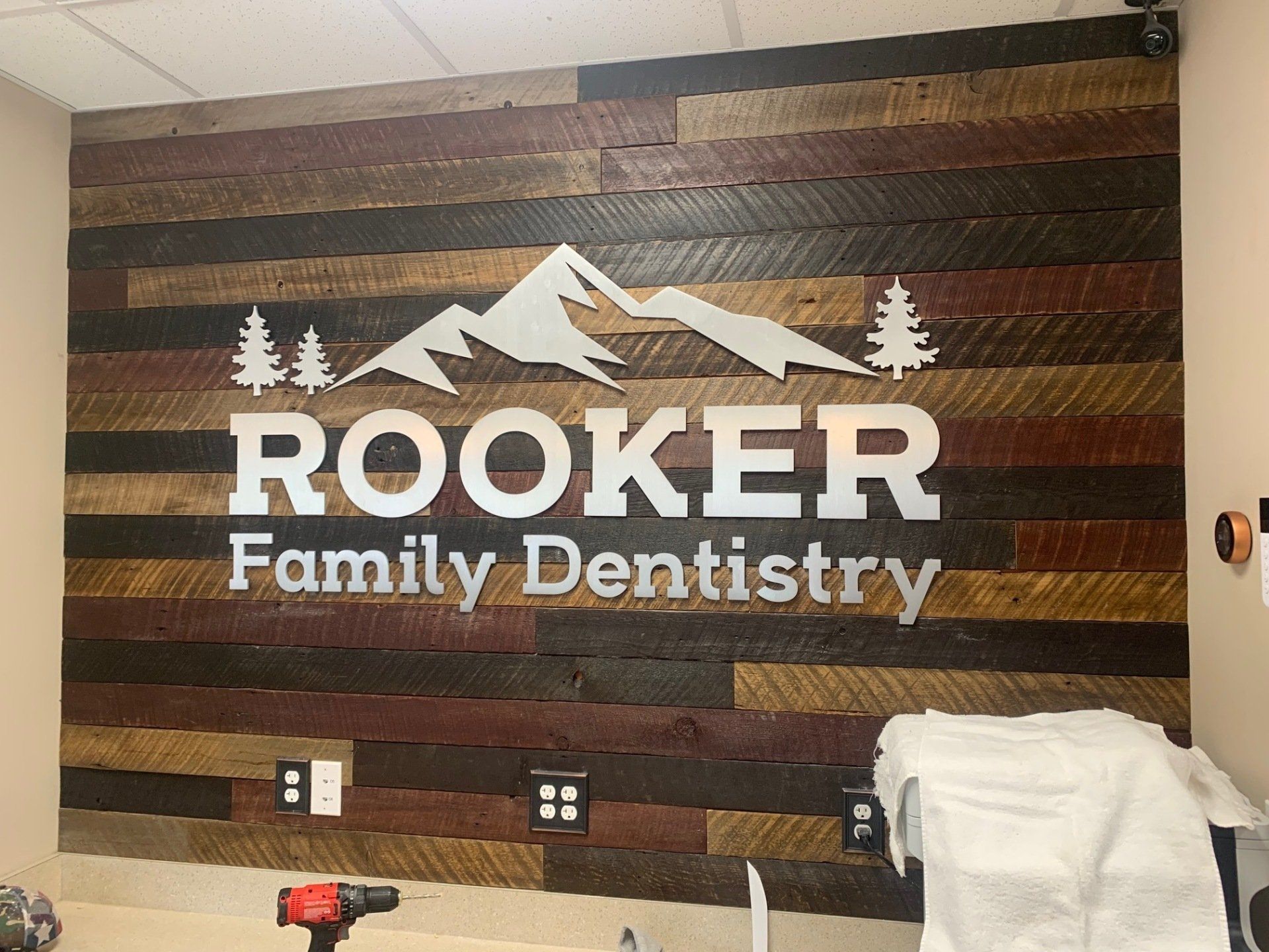 A sign for a family dentistry is hanging on a wooden wall.