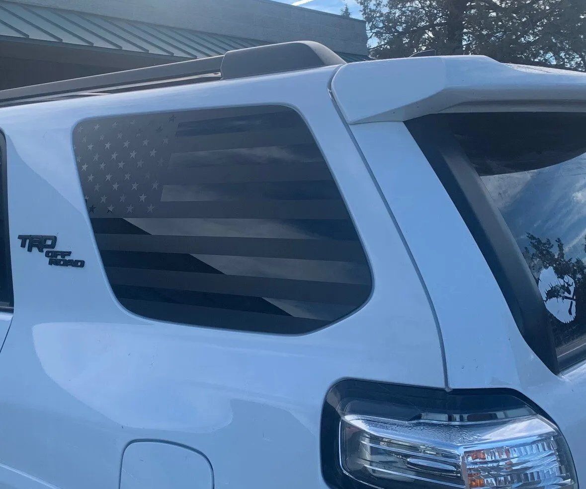 A white suv with an american flag on the window is parked in front of a building.