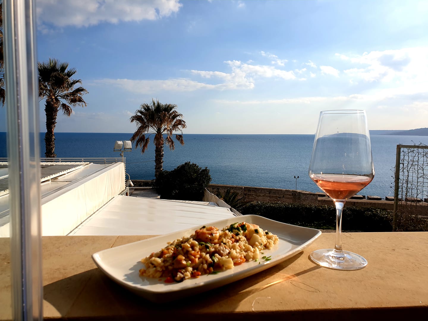 risotto ai frutti di mare e calice di vino rosato con mare sullo sfondo