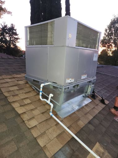 Rooftop HVAC unit on a shingled roof, with white PVC piping.