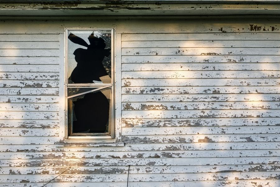 A window broken and shattered by extreme heat from a nearby wildfire, showing secondary structural damage