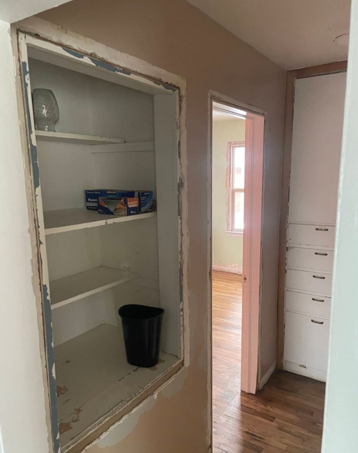 Hallway with old built-in cabinet and damaged drywall being prepped for renovation