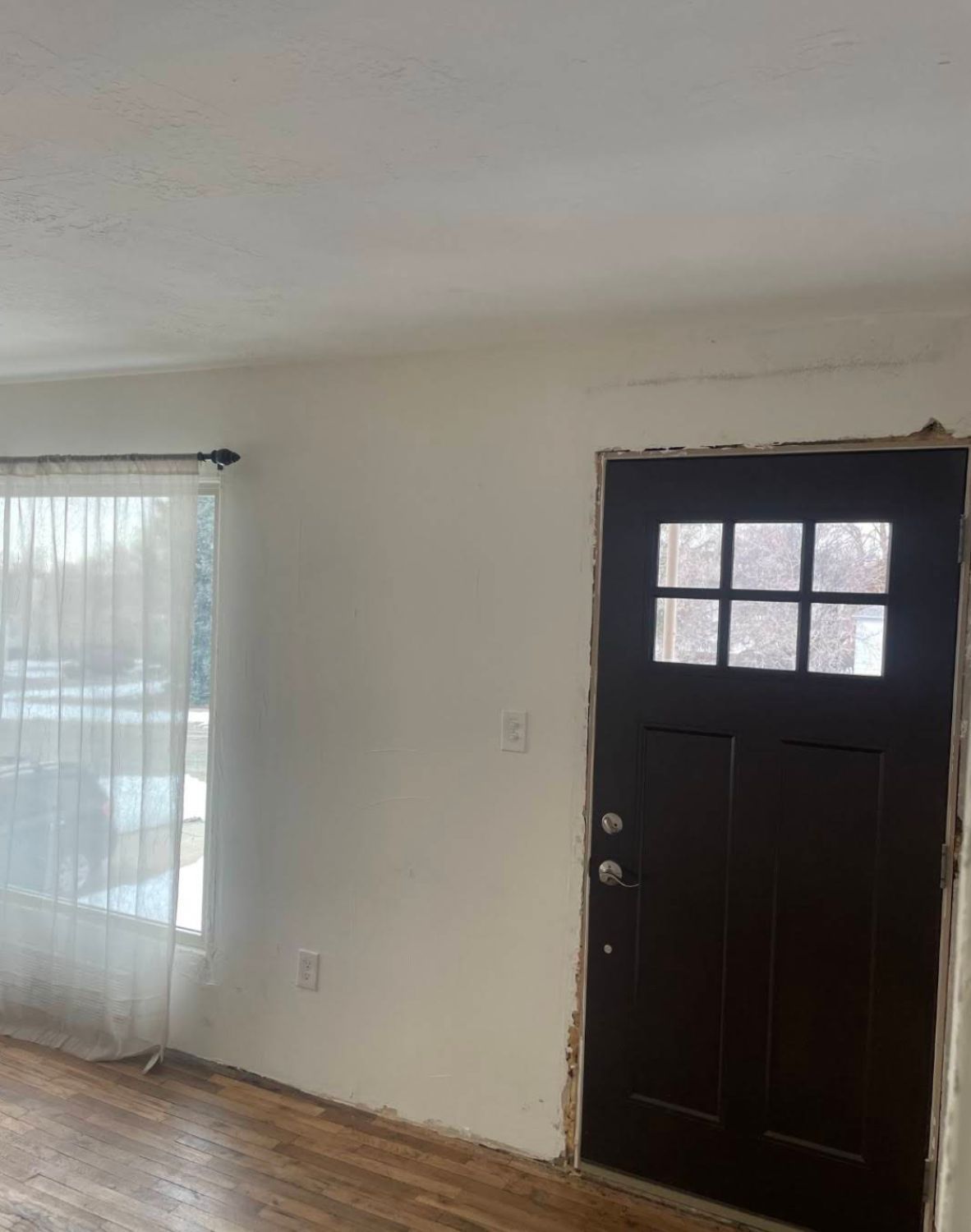 Kitchen during demolition showing black refrigerator and gray walls with tile backsplash partially removed