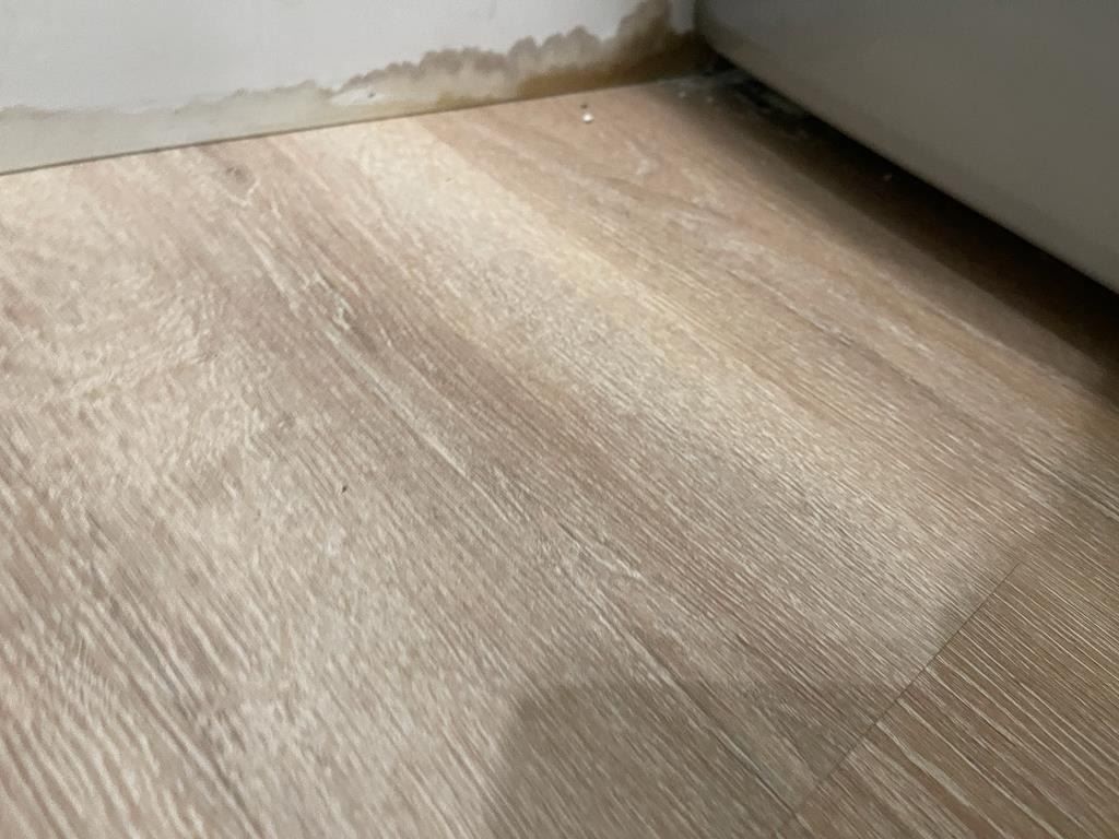 Kitchen flooring destroyed by sewage backup showing exposed subfloor and debris
