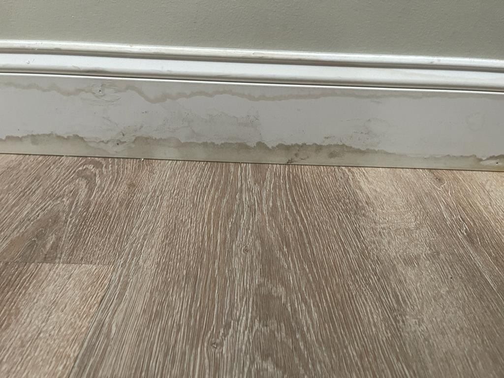 Sewage damage near pipes and flooring at base of wall in condo unit
