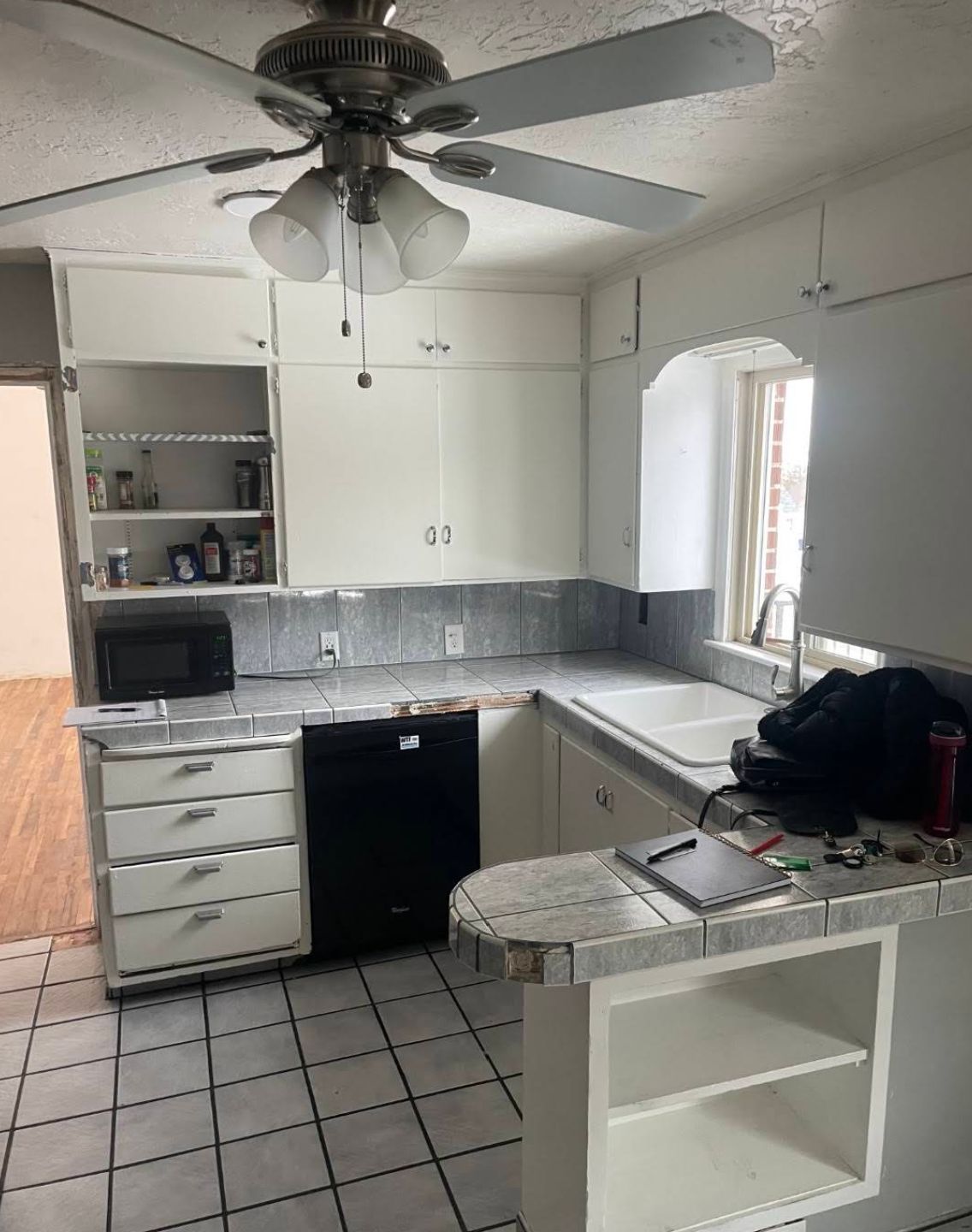 Kitchen sink area with dated tile backsplash and worn cabinets before renovation