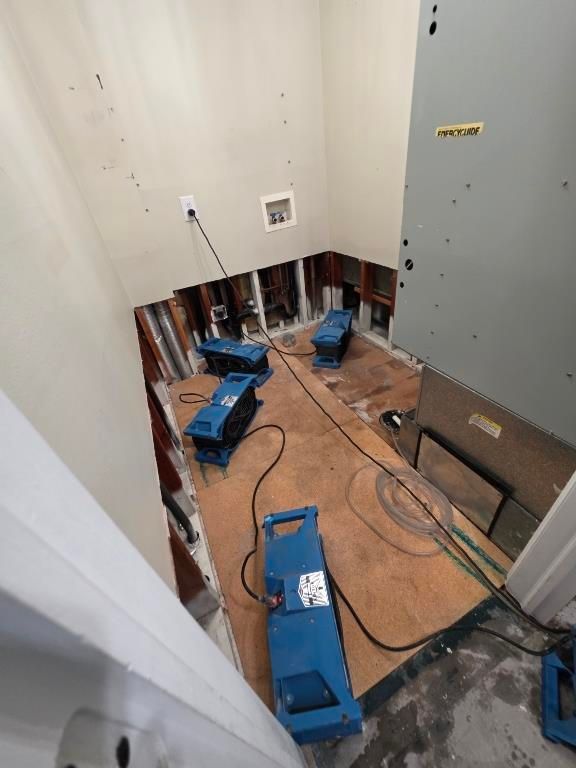 Bathroom stripped to subfloor and studs with plumbing exposed during drying process