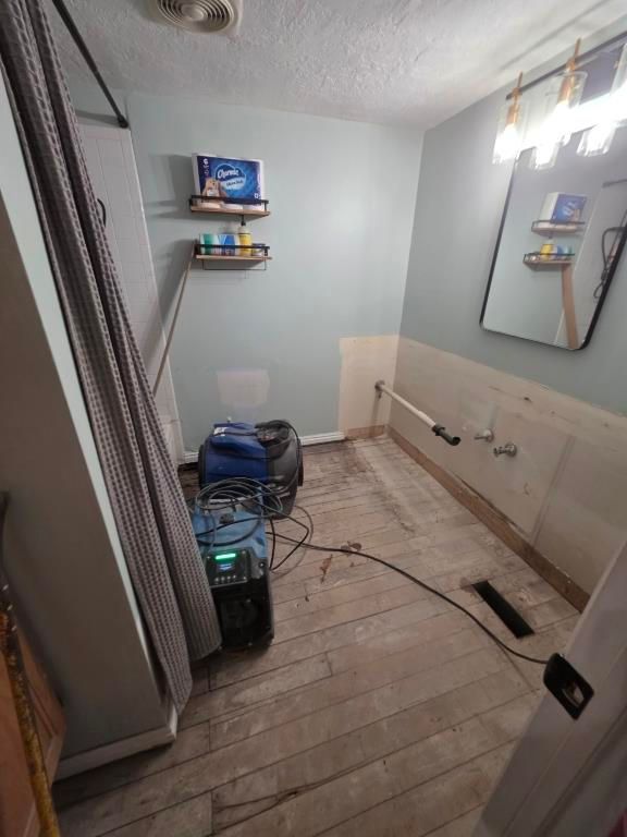 Industrial dehumidifier running in stripped bathroom during structural drying phase