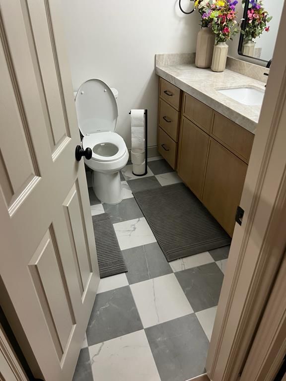 Restored bathroom with new checkered tile flooring, wood-tone vanity, and stone countertop