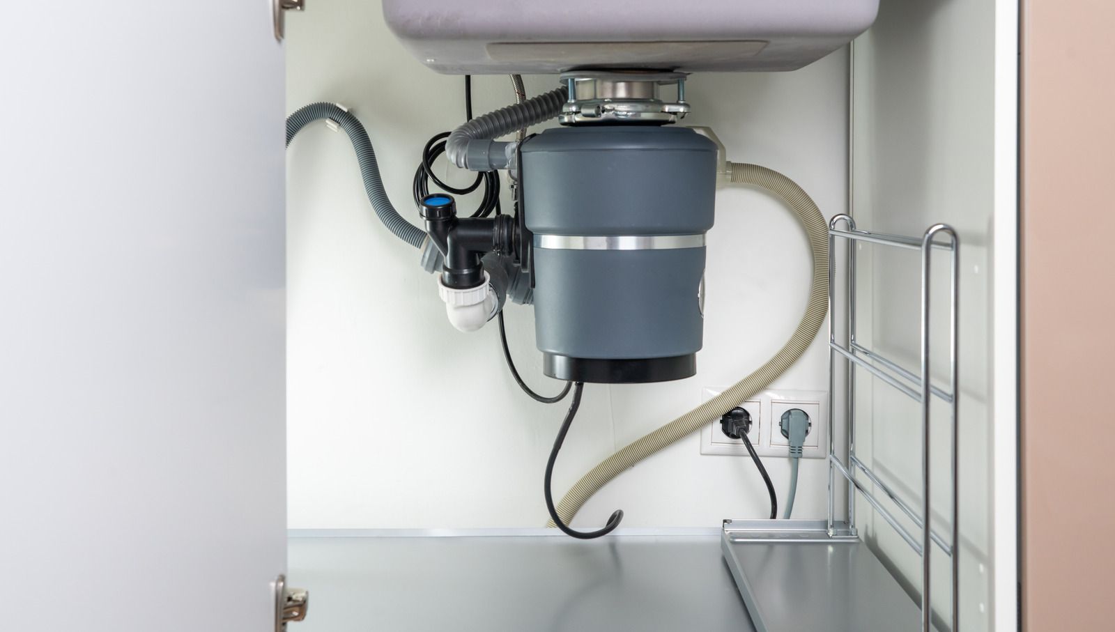 Garbage disposal unit under a kitchen sink, with pipes, wiring, and a power outlet.