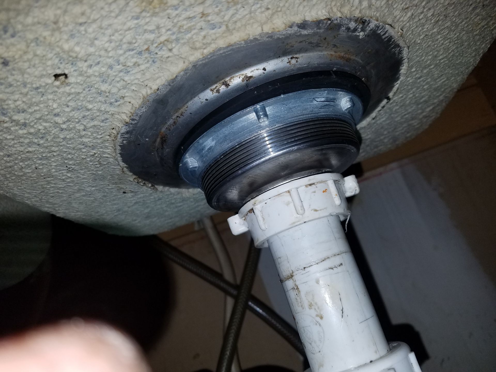 Underside of a sink drain assembly with a threaded metal section and a connected white plastic pipe.