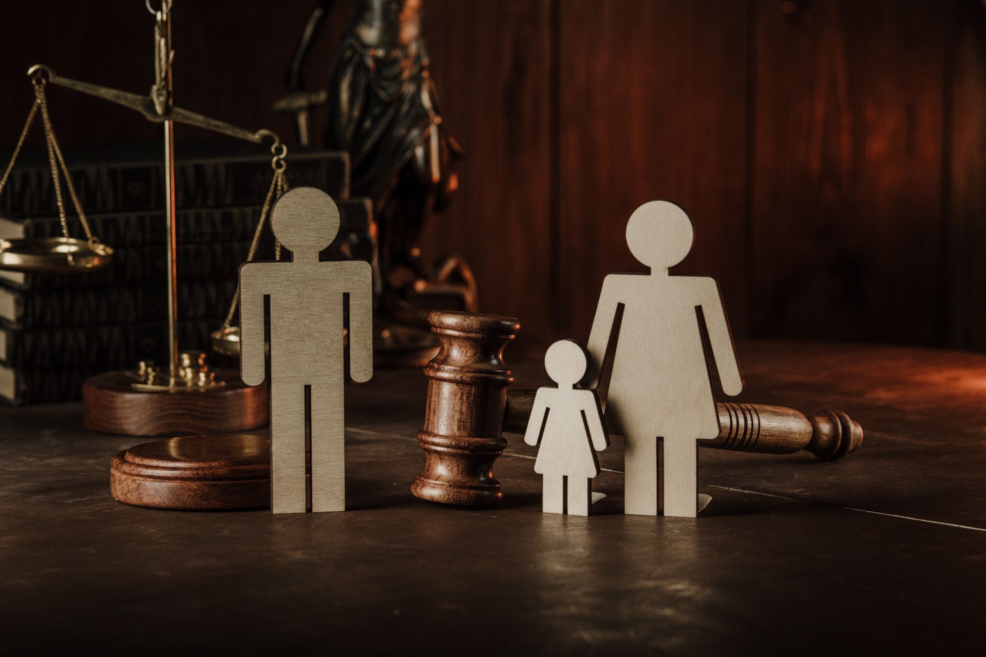 Wooden family figures beside a gavel, scales of justice, and law books on a desk