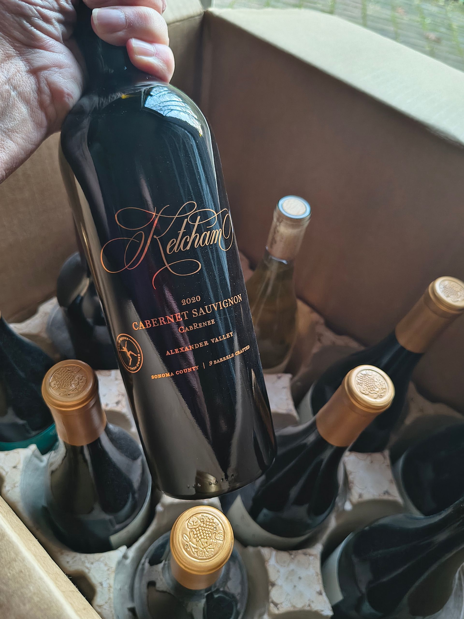 Hand placing a black wine bottle in a box of assorted bottled wine with gold caps